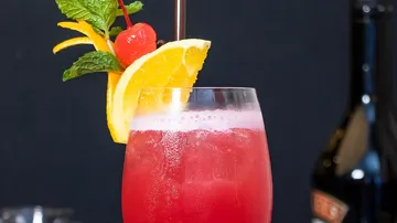 Roter Cocktail mit Orangendekoration, schwarzer Hintergrund.