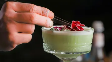 Hand garniert grünen Cocktail mit Blumen.