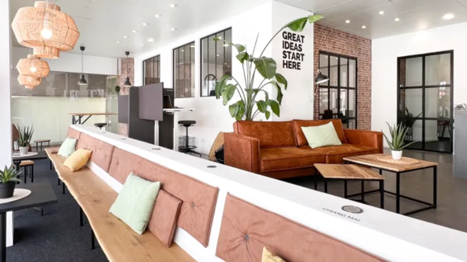 Modern office with sofa and plants, bright lighting.