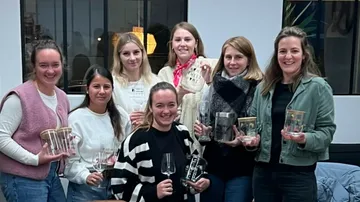 Seven women holding various trophies indoors.