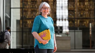 Woman smiling, holding yellow bag in church.