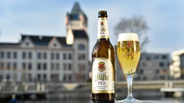 Beer bottle and glass beside historical building.