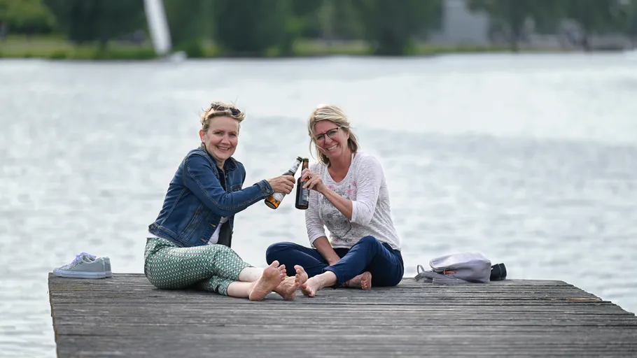 Two women sitting on a dock, holding drinks.