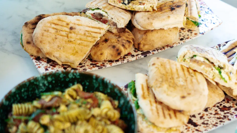 Grilled sandwiches and pasta salad on a table.