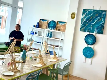 Kunststudio mit Staffeleien, Gemälden und Person.