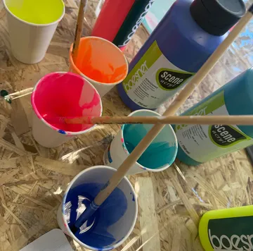 Pinsel in Bechern, bunte Flaschen daneben.