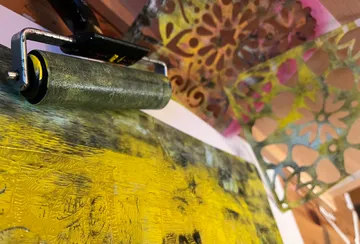 Paint roller applying yellow paint on canvas.