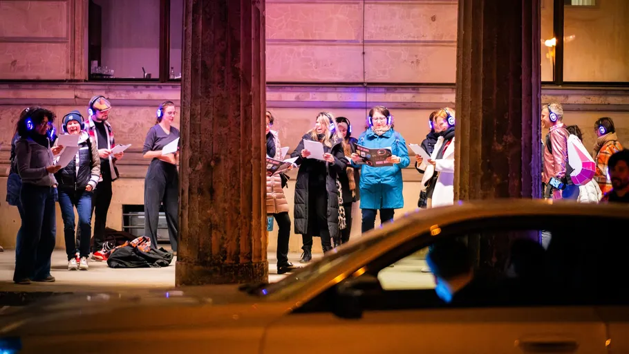 Group wearing headphones singing, urban street setting.