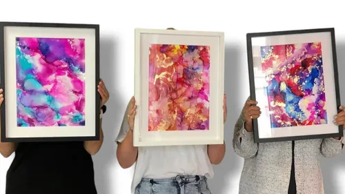 Three people holding colorful framed artwork.