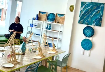 Kunststudio mit Staffeleien und Gemälden, Person sitzt.