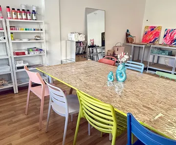 Raum mit bunten Stühlen, Kunstmaterialien und Tisch.