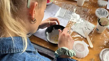 Person mixing in a bowl on cluttered table.