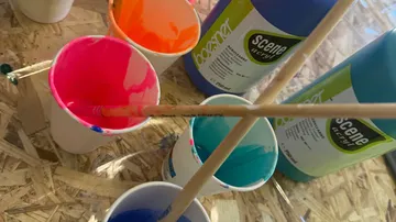 Becher mit Farbe und Pinseln auf einem Tisch.