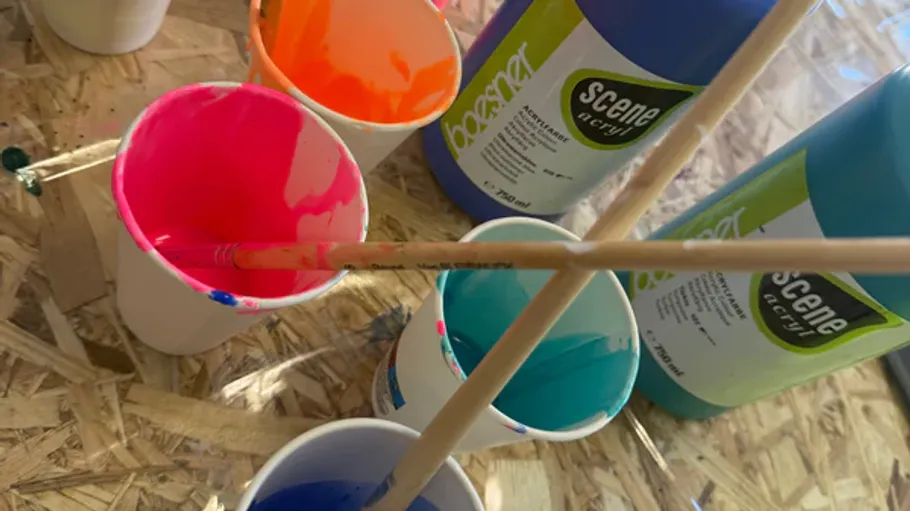 Becher mit Farbe und Pinseln auf einem Tisch.