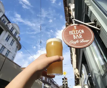 Hand holding beer beneath blue sky with sign.