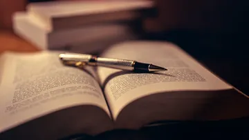 Offenes Buch mit Stift darauf, schummrig beleuchtet.