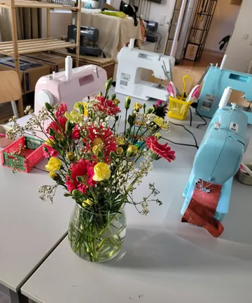 Flowers in vase beside sewing machines in workshop.