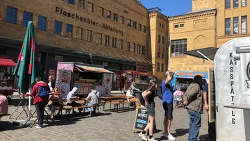 People eating at outdoor food stalls, brick building.