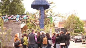Gruppe beobachtet riesige blaue Pilzskulptur draußen.