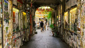 People walking through graffiti-covered alley with shops.