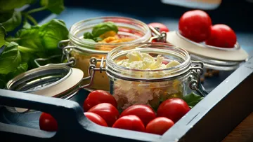 Gläser mit Käse und Tomaten auf Tablett.