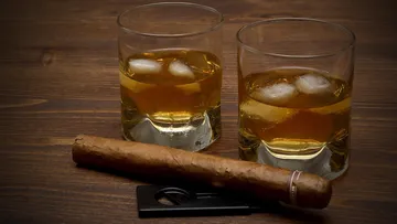 Two whiskey glasses and a cigar on table.