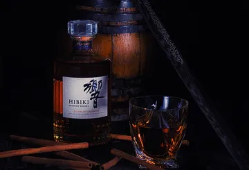 Whisky bottle and glass beside barrel and sword.