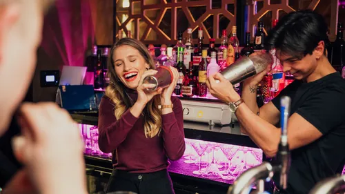 Zwei Barkeeper lächeln, schütteln Cocktailshaker.