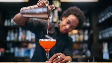 Barkeeper gießt Cocktail aus Shaker ins Glas.