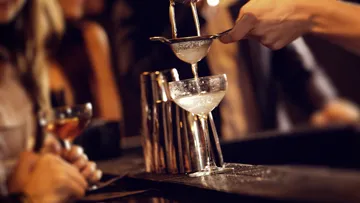 Bartender straining cocktail into glass at bar.