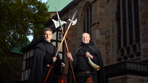 Two men in cloaks holding weapons, medieval building.