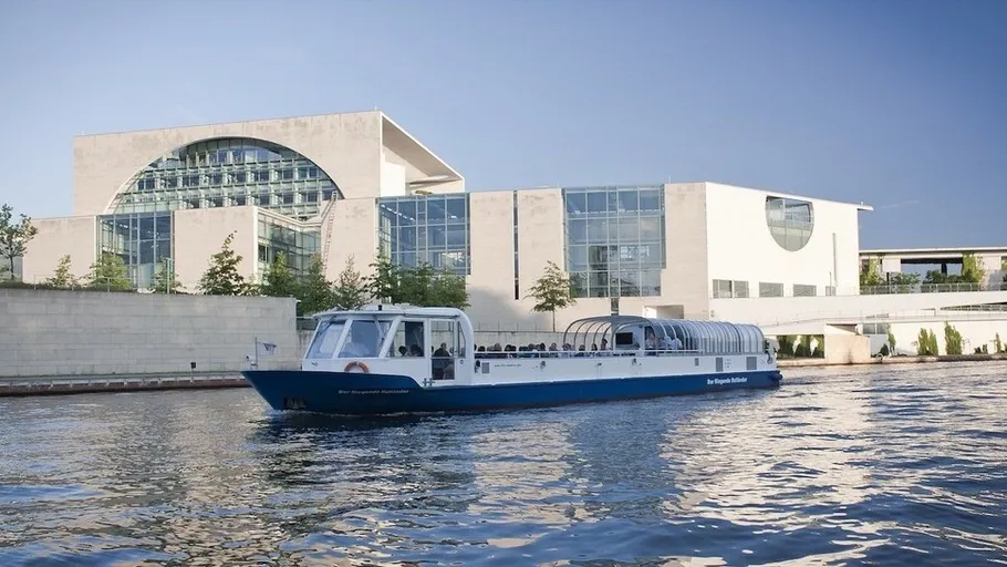 Touristenboot passiert Regierungsgebäude am Fluss.
