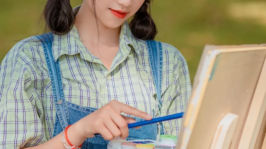 Woman painting canvas outdoors in daylight.