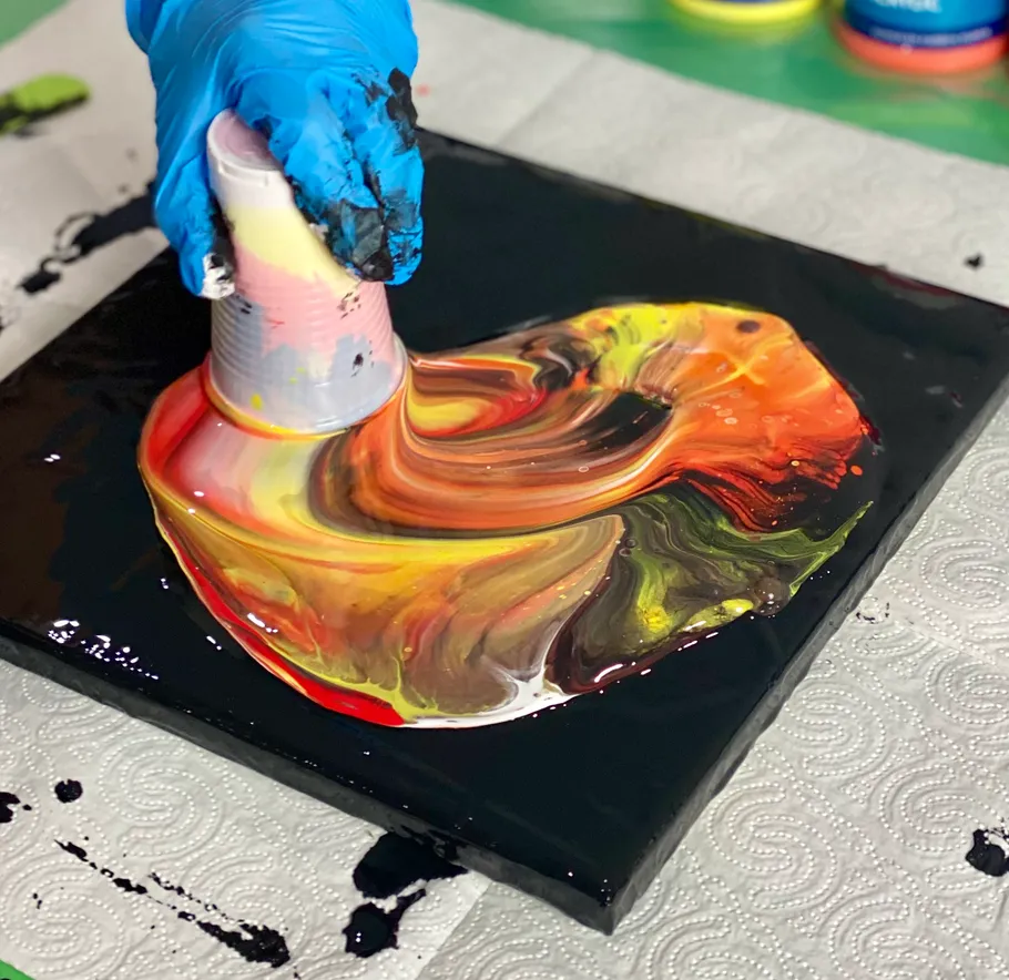 Gloved hand pours colorful paint on canvas.