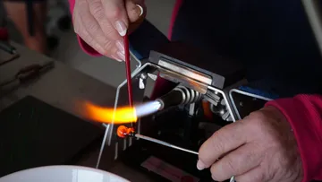 Hände formen Glas über einer kleinen Flamme.