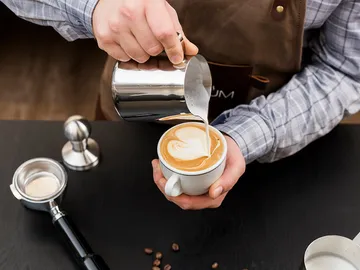 Barista gießt Milch in einen Cappuccino in einer Tasse.