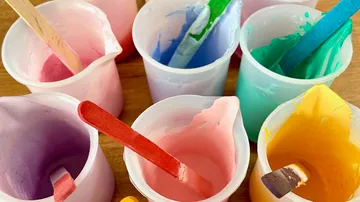 Bunte Farben in Plastikbechern mit Stäbchen.