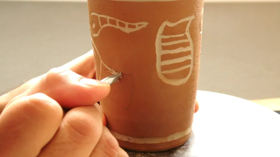 Hand etching design on a clay cup.