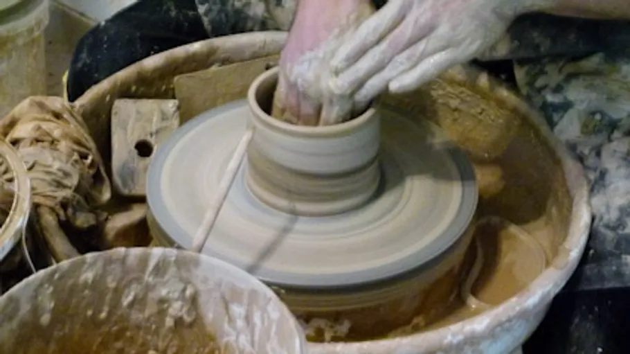 Hands shaping clay on spinning pottery wheel.