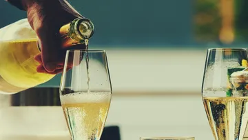 Hand gießt Champagner in zwei Gläser.