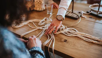 People crafting macramé on wooden table.