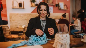 Woman working with blue yarn in cozy room.