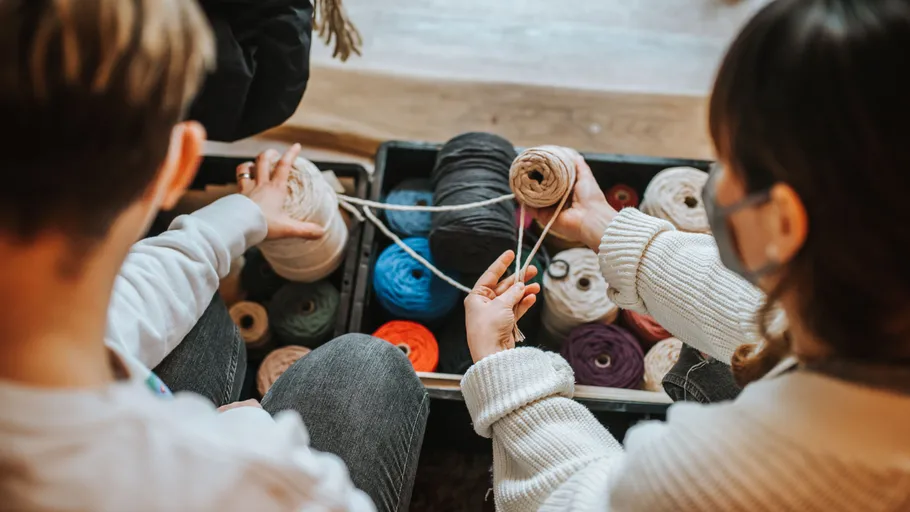 Two people selecting colored yarn in a box.