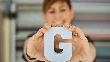 Person hält Buchstaben 'G' mit verschwommenem Hintergrund.
