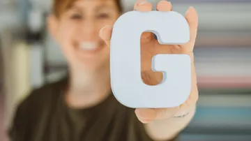 Person hält Buchstaben G mit Lächeln.