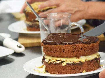 Kuchen wird mit Schokoladenüberzug in einer Küche dekoriert.