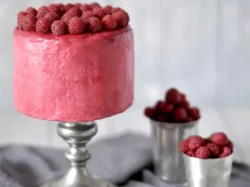 Himbeertorte steht auf einem silbernen Ständer, umgeben von Beeren.