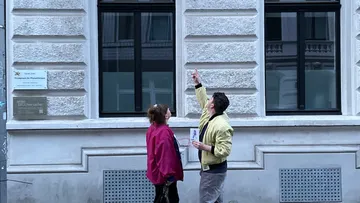 Zwei Personen blicken zur Gebäude-Fassade auf.