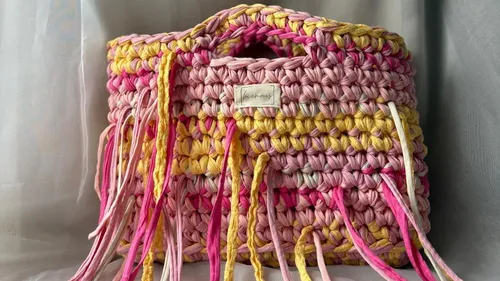 Bunte gehäkelte Tasche mit Fransen im Raum.