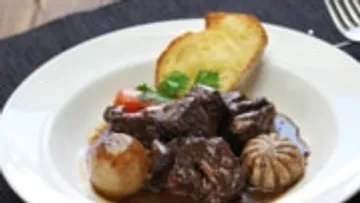 Rindereintopf mit Zwiebeln und Brot auf Teller.